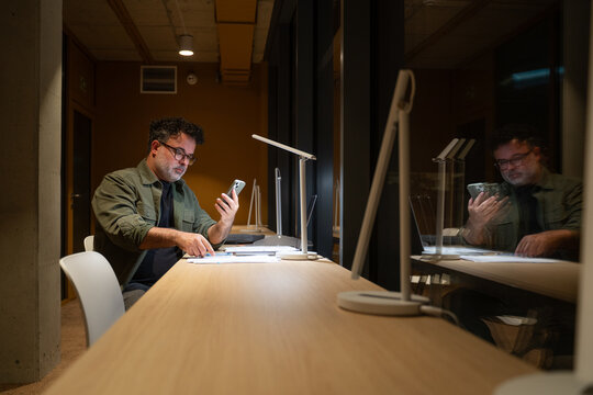 Businessman Using Phone At Office Desk At Late Night
