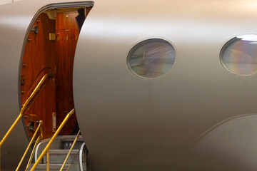 Fototapeta premium Open cabin door gulfstream g boarding stairs extended into hangar, illuminated threshold, polished step rails and warm interior wood contrast with exterior shell
