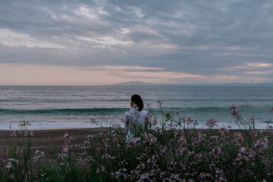 A woman gazing at the sea from in front of a flower patch.