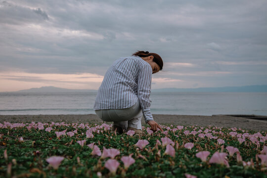 A woman crouching in a flower patch on the beach at dusk.