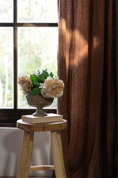Pretty flowers in a vintage urn on a stool in a window