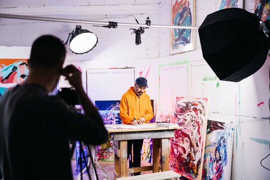 Artist drawing at workbench under filming setup

