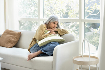 Menopause and tension. Middle-aged woman curled up on couch, hugs pillow, suffers from of emotional...