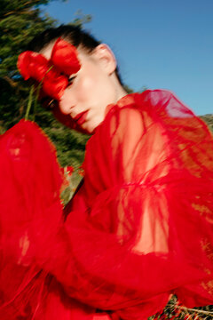 Model posing with red poppy flower and red tulle dress 