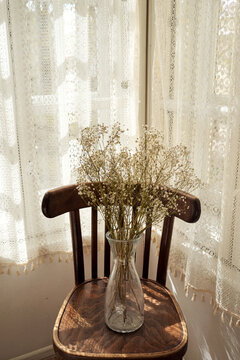 Flowers arranged in a glass vase on a wooden chair