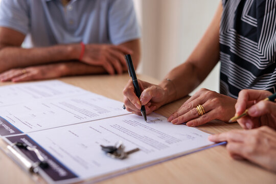 Buyer signing real estate contract with keys on table
