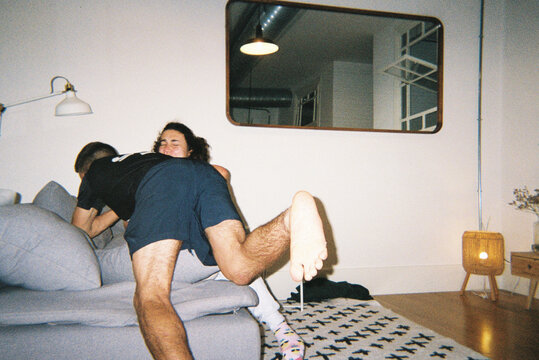 Playful friends wrestling on the couch at home
