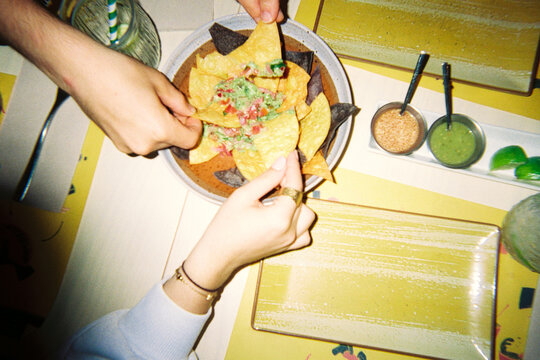 Hands sharing nachos with guacamole and salsa
