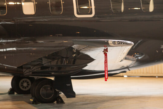 Gulfstream G wheel closeup in hangar showing polished fuselage and red removebeforeflight tag, reflective chrome surfaces, maintenance lighting and careful preflight inspection,