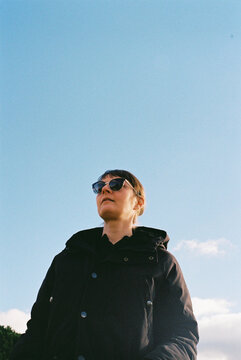 Woman Wearing Sunglasses Stands Against Clear Blue Sky