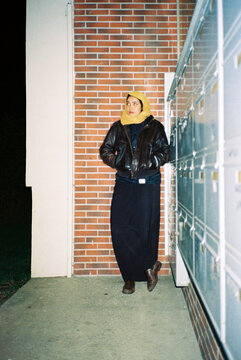 Woman in Jacket and Scarf Stands by Mailboxes at Night