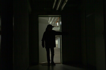 teen boy silhouetted at exit threshold, hand on handle, backlight casting long shadow across industrial corridor, tense atmosphere of decision and cautious exploration.