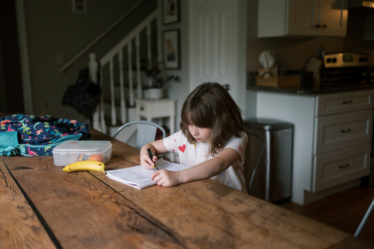 young child sitting at table after school and drawing on notebook