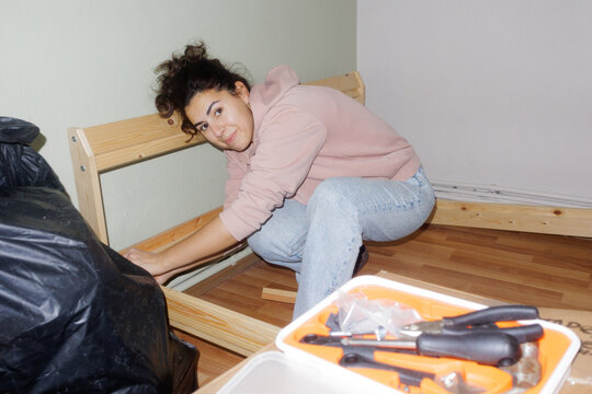 A young woman is disassembling a bed frame
