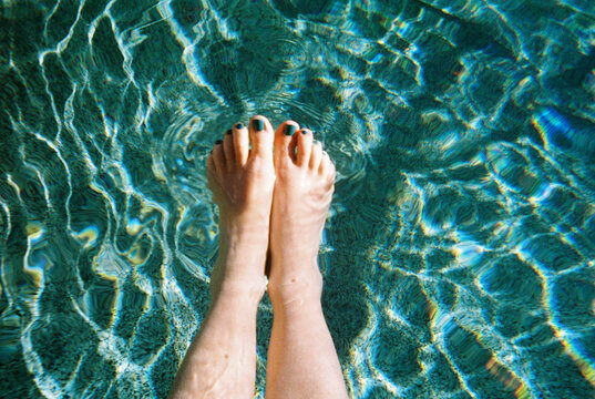 Woman's feet dipping into blue green pool water