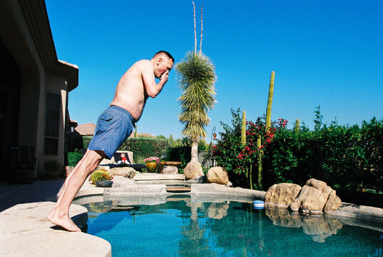 Candid film photo of man doing bellyflop into backyard swimming pool