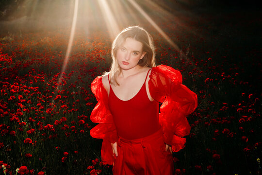 Model posing in poppy field at sunset with sun rays and flash light