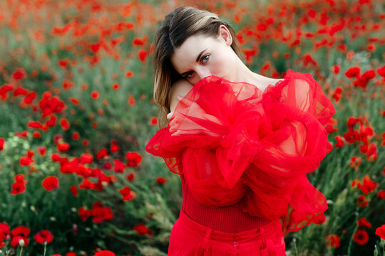 Fashion model hiding her face with red dress in poppy field