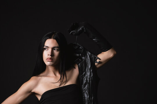 Nonbinary model wearing black top holding leather coat 