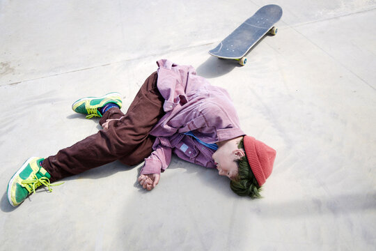 Skateboarder falls while practicing tricks at a sunny skate park