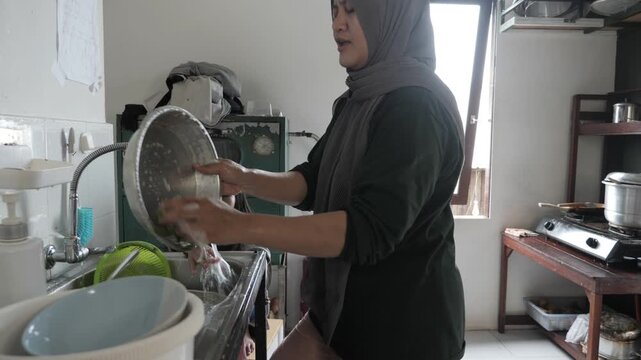 Asian muslim mother washing dish and kitchenware with her little daughter, childhood and parenting. Natural real life scene
