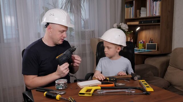 A loving and thoughtful father demonstrates a variety of tools to his young son while they are seated at the dining table. The father is imparting knowledge to his son.