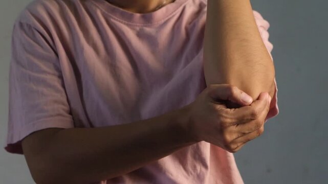 A woman is experiencing elbow pain and discomfort. She is holding her arm and looks to be in pain. The footage can be used to illustrate arm injuries, inflammation, or general discomfort.