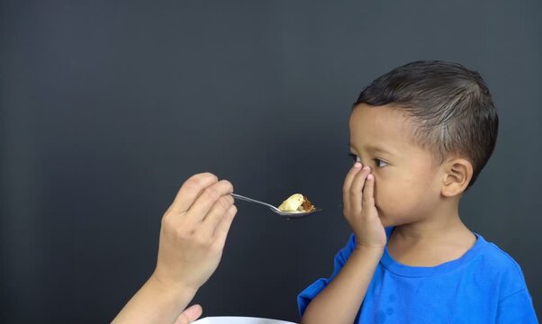 A small Asian boy is covering his mouth with both hands, a gesture of not wanting to eat anymore, known as GTM (Closed Mouth Movement), not wanting to continue eating from his mother