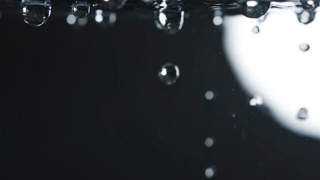 Close-up slow-motion video of water droplets falling against a dark background from top view