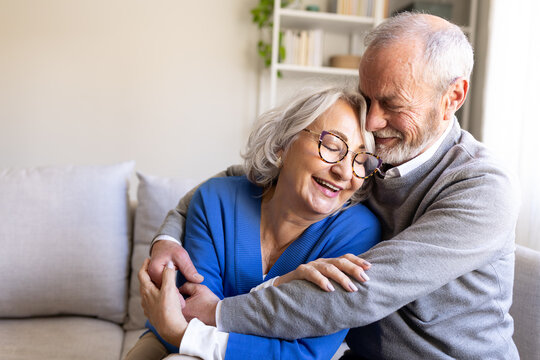 Happy senior couple embracing on sofa at home, enjoying retirement