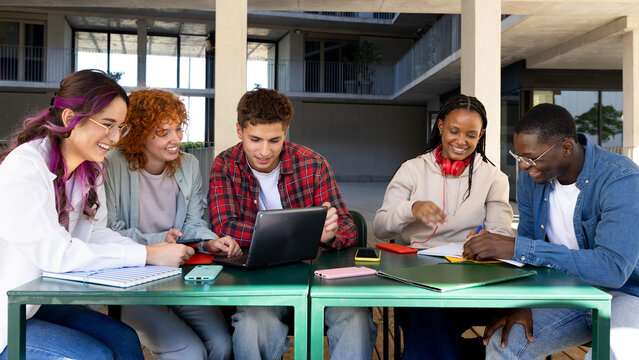 University students collaborating on project outdoors using laptop and notebooks