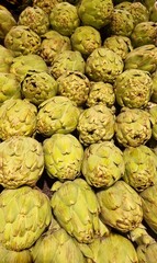 Obraz premium Fresh green artichokes are stacked closely together on a shelf, likely in a supermarket. The artichokes have a layered, scaly appearance with tightly packed leaves, displaying a bright green color