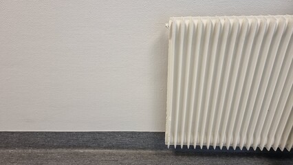 A radiator water heater for heating a room with figured milky waves hanging next to a white wall. 