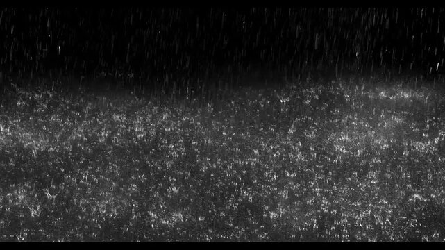Realistic rain drops hitting the ground creating beautiful water splashes on a dark black background. Perfect cinematic rain overlay for video editing, visual effects, films, trailers, music videos