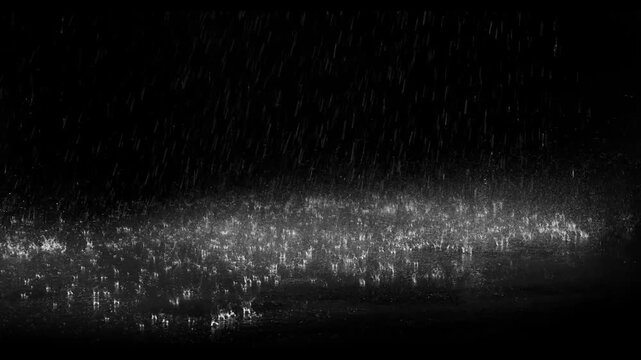 Realistic rain drops hitting the ground creating beautiful water splashes on a dark black background. Perfect cinematic rain overlay for video editing, visual effects, films, trailers, music videos