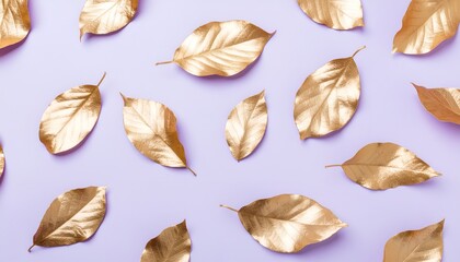 Fototapeta premium A collection of gold-painted leaves arranged artistically on a soft lavender background