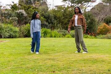Two African American teenage girls standing on green turf in park near flowers, wearing headband