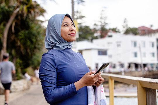 Filipina woman walking on coastal path holding a phone and a towel on the other hand