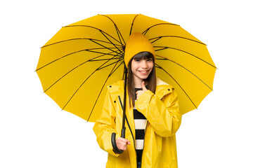 Little girl with rainproof coat and umbrella over isolated chroma key background giving a thumbs up gesture © luismolinero