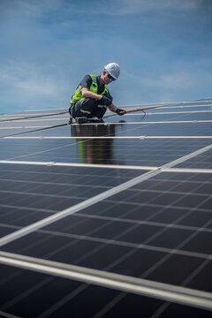 Technician installing solar panels on factory roof for green energy. A skilled technician in safety gear is working on a solar panel installation on rooftop.