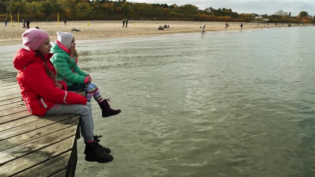 Two little beautiful girls sit on wooden pier
