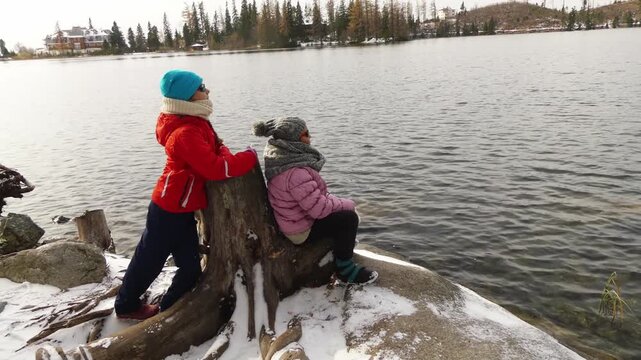 Two little beautiful girls walk along shore of winter lake of Strbske Pleso, is favorite ski, tourist, and health resort in High Tatras, Slovakia.