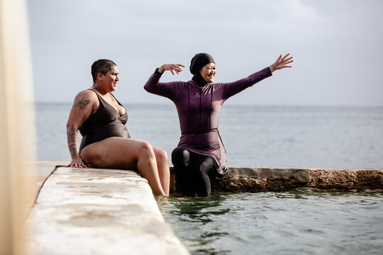 Playful Mixed-race women sitting on stone platform of the tidal pool