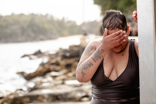 Woman with tattoos standing under an outdoor shower wiping water from her face