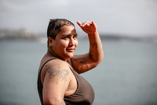 Woman with tattoos standing in the poolside shielding eyes from the sun