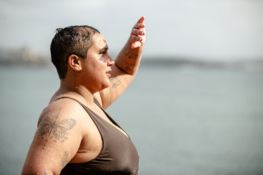 Woman with tattoos standing in the poolside shielding eyes from the sun