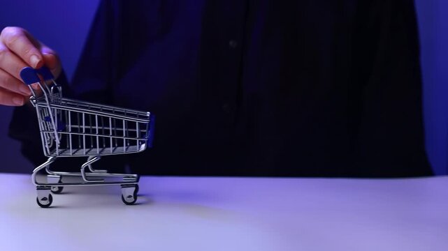 Hand placing object in small shopping cart on table in indoor space during evening hours.