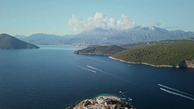 Aerial view of Mamula Island fort near Montenegro, speedboats cross the bay leaving white wakes, turquoise shallows and rocky coast appear under clear daylight