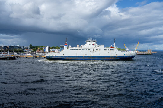 Horten, Norway - August 27 2023: passenger ferry departing coastal harbor under stormy sky.