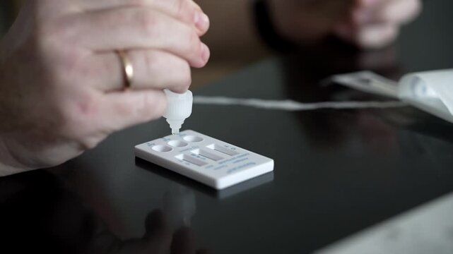 Close-up of person applying liquid solution to a rapid test cassette for respiratory viruses at home, demonstrating self testing process.

